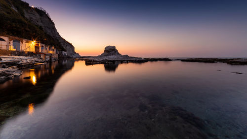 Sea by illuminated buildings against sky during sunset