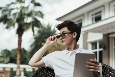 Man holding digital tablet standing against house