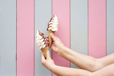 Cropped hands holding ice cream cones against wall