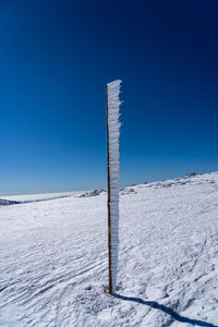 Wooden post on snow covered field against clear blue sky