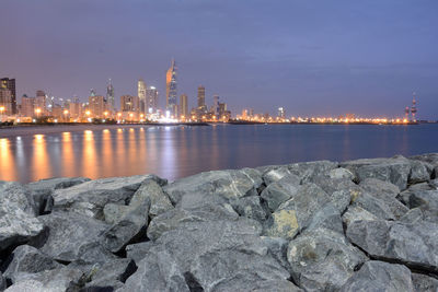 Sea by illuminated buildings against sky at night