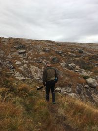 Rear view of man walking on landscape against sky