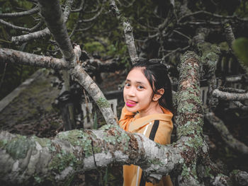 Portrait of young woman against tree trunk