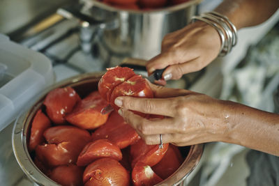 Cropped hands of woman cutting tomato in kitchen