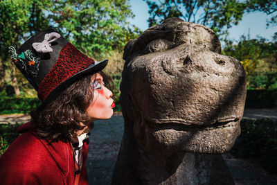 Portrait of man cosplaying mad hatter kissing statue