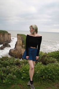 Woman standing on cliff at beach against sky