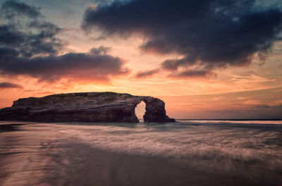 Rock formation on beach against sky during sunset