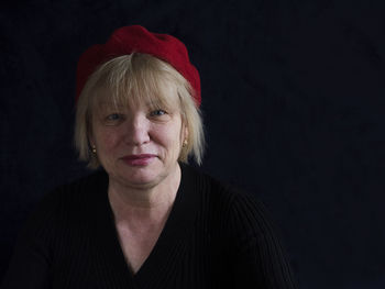 Portrait of smiling mature woman with red cap against black background