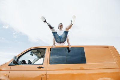 Happy young man with leg prosthesis balancing on roof of camper van