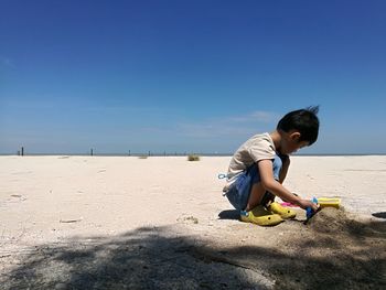 Boy playing on sand at beach against sky