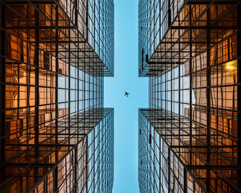 Directly below shot of modern buildings and airplane against blue sky
