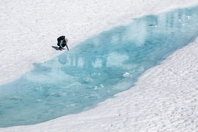 Drone view of unrecognizable female hiker resting and putting hand in melting lake with clear blue water during vacation in british columbia