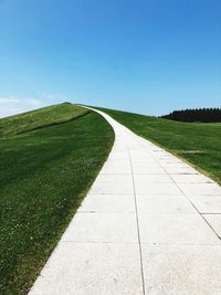 Empty road amidst field against clear sky