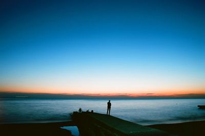 Silhouette people on beach against clear sky during sunset
