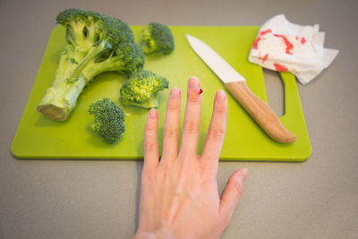 Cropped hand of woman with blood on finger by vegetables on cutting board