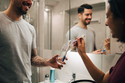 Smiling couple arranging toothbrushes in container by mirror in bathroom