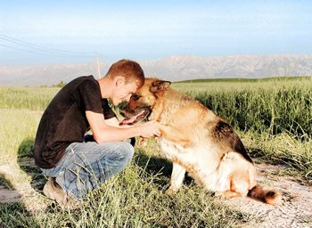 Man with dog sitting on field against sky