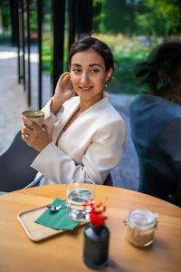 Smiling friends using mobile phone while sitting at table