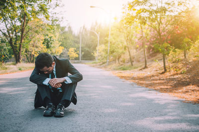 Full length of man sitting on road by trees