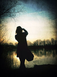 Silhouette of people standing by lake at sunset