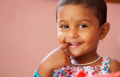 Close-up portrait of girl with finger in mouth against peach wall