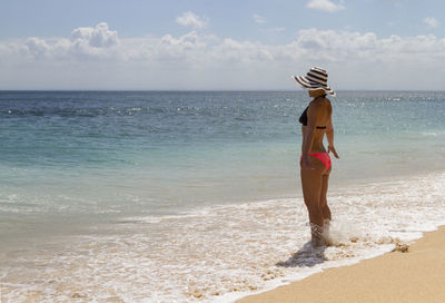 Rear view of young woman walking on beach against sky