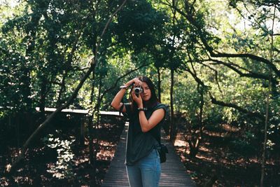 Full length of woman taking photo by tree against sky