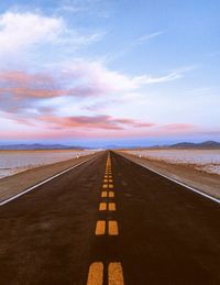 Empty road leading to sea against sky