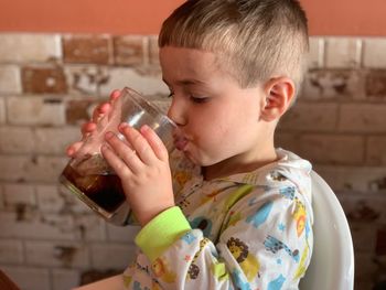 Close-up of boy drinking juice while sitting on high chair against wall