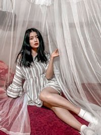 Portrait of young woman sitting in curtain