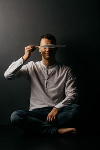 Full length portrait of young man sitting against black background