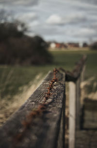 Close-up of rusty metal railing on field against sky