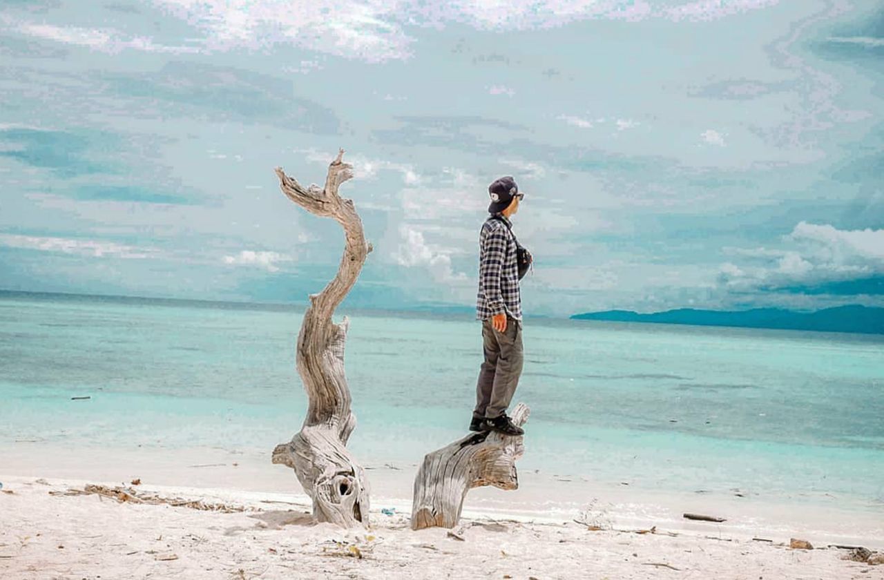 MAN STANDING ON BEACH AGAINST SKY