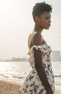 Side view of woman with short hair standing at beach against clear sky