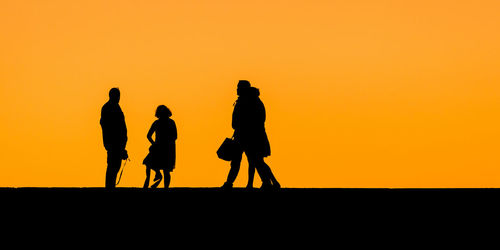 Silhouette men against orange sky