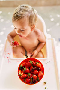 Smiling baby girl sitting while eating strawberry at home