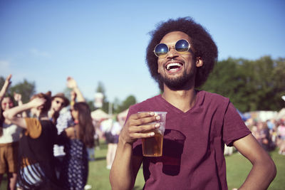 Cheerful young man holding beer while standing in party during sunny day
