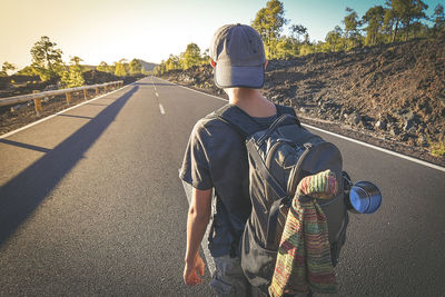 Rear view of boy with backpack walking on road during sunset