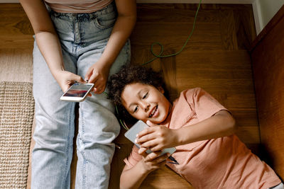 Smiling boy using smart phone with sister while lying down on floor at home