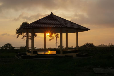 Gazebo on field by building against sky during sunset