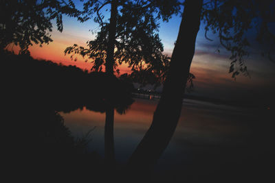 Silhouette trees by lake against sky during sunset