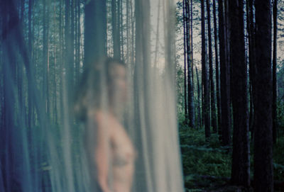 Woman standing by tree trunk in forest