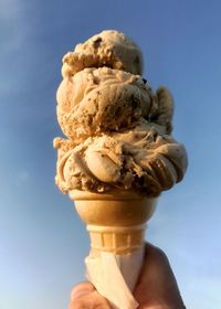 Human hand holding ice cream against sky