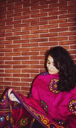 Woman looking away while sitting against brick wall