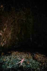 From above of unrecognizable relaxed female traveler in bikini lying on water surface of clear transparent pool near rock cave while enjoying summer vacation in rincon de la vieja national park in costa rica