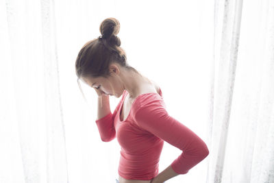 Side view of woman looking down while standing by curtain at home