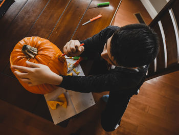 High angle view of boy making jack o' lantern of fresh pumpkin while sitting at table