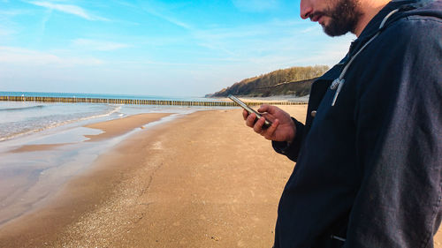 Midsection of man using smart phone at beach against sky