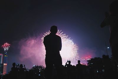 Rear view of silhouette people looking at firework display in sky at night