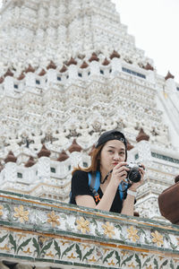 Portrait of young woman looking at temple against building